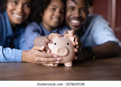 Joyful African Family Young Couple Parents And Little Child Girl Holding Piggybank In Hands, Feeling Excited Of Saving Money, Planning Future Expenditures, Learning Managing Budget At Home.