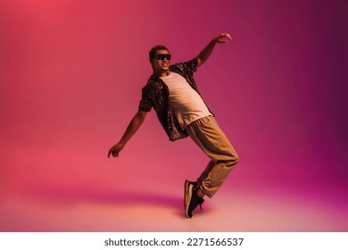 Joyful african man wearing sunglasses   leopard shirt dancing isolated over pink neon background