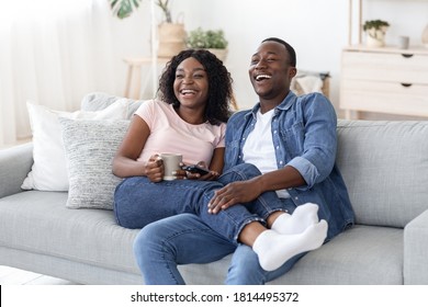 Joyful african man and woman drinking tea and watching movie at home, having fun together, copy space