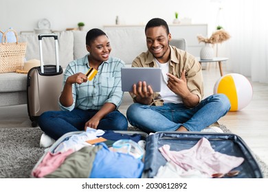 Joyful African Tourists Couple Booking Tour Online With Digital Tablet And Credit Card, Browsing Internet And Purchasing Travel Tickets Together At Home. Travel Services And Applications Concept