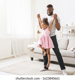 Joyful Afro Girl In Beautiful Pink Dress Playing With Her Dad, Father Lifting Little Daughter Up, Home Interior, Copy Space