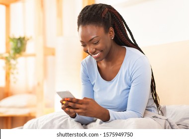 Joyful Afro Lady Using Cellphone Playing Mobile Games Sitting In Bed At Home. Selective Focus