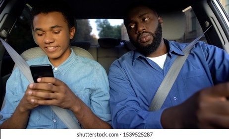 Joyful Afro-american Teen Texting Phone Dad Trying To Read Message While Driving