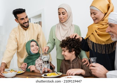 joyful arabian woman poring tea during dinner with interracial muslim family