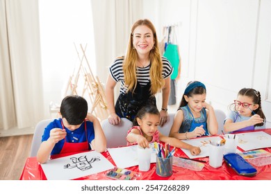 Joyful art instructor observing children painting with watercolors and enjoying themselves in art class at the school - Powered by Shutterstock