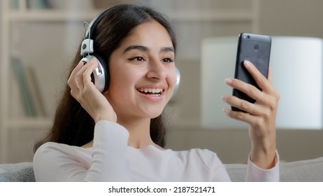 Joyful artistic arabic woman teenager wears headphones earphones listen music melodies choose audio track in mp3 playlist dynamic move hands enjoy musical hobby rest weekend at home sing favorite