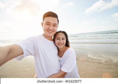 Joyful Asian couple taking photograph on the beach - Powered by Shutterstock