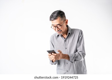 A Joyful Asian Elder Man In A Gray Stripe Shirt Uses A Cell Phone For Texting Or Social Media. On White Background In A Studio. Positive Active Old Cool Senior Healthy Retirement Concept. Copy Space.