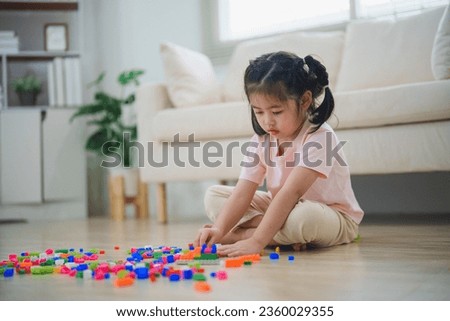 Joyful Asian girl happy and smiling playing colorful toy block, sitting on the living room floor, creatively playing with block, building colorful structures creativity imagine. Learning education.