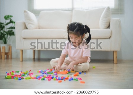 Joyful Asian girl happy and smiling playing colorful toy block, sitting on the living room floor, creatively playing with toy, building colorful structures creativity imagine. Learning education.