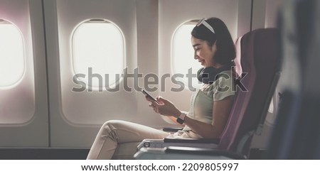 Joyful asian woman sits in the airplane and using mobile phone while go to travel