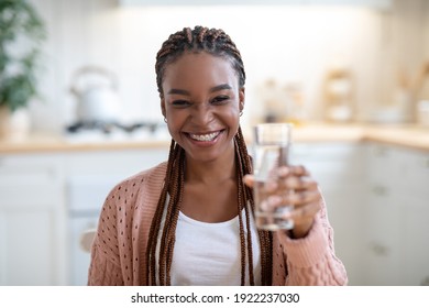 Joyful Attractive Black Lady Holding Glass With Water, Offering Refreshing Drink To Camera, Smiling African American Woman With Braces Posing With Healthy Liquid In Kitchen Interior, Free Space - Powered by Shutterstock