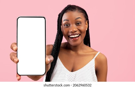 Joyful attractive black woman with dreadlocks recommending mobile app on smartphone with blank screen, mockup, cheerfully smiling at camera, pink studio background, panorama with copy space - Powered by Shutterstock