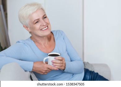 Joyful attractive mature woman relaxing at home, drinking coffee, copy space