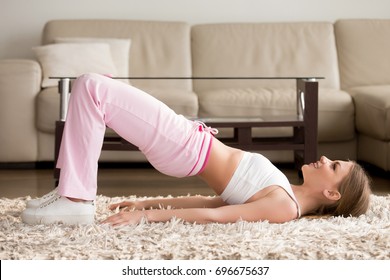 Joyful Attractive Young Woman Lying On Floor In Living Room And Doing Hip Bridge Exercise. Happy Smiling Lady In Sportswear Lifting Pelvis On Carpet, Enjoying Physical Activity And Fitness At Home