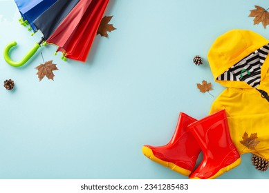 Joyful autumnal ambiance with rain for kids. Capture a top view photo showcasing a colorful umbrella, raincoat and gum boots on a blue isolated background, perfect for text or ads