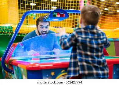 Joyful Bearded Father And Son Playing Air Hockey Game At Amusement Park