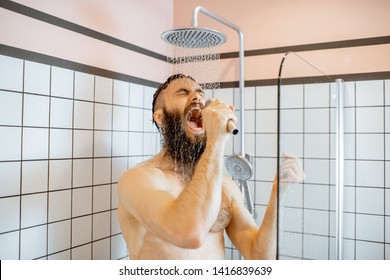 Joyful bearded man singing into the micrphone while taking a shower in the bathroom