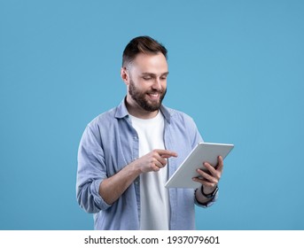Joyful bearded man using tablet computer for online work or studies on blue studio background