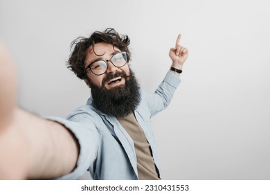 Joyful bearded man wearing eyeglasses and denim shirt taking selfie against white background - Powered by Shutterstock