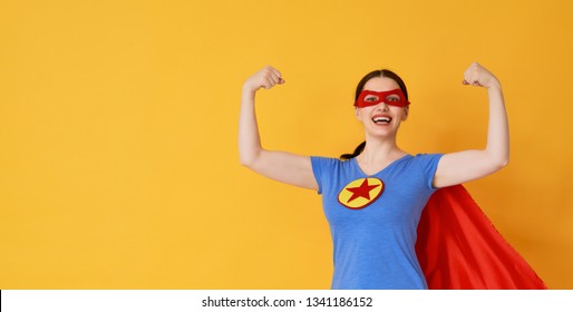 Joyful beautiful young woman in superhero costume posing on yellow background.