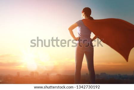Joyful beautiful young woman in superhero costume posing on sunset background.