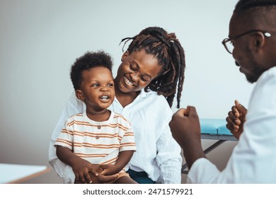 A joyful black boy sits on his mother's lap during a medical consultation as the doctor engages them in conversation, ensuring a soothing healthcare environment. - Powered by Shutterstock