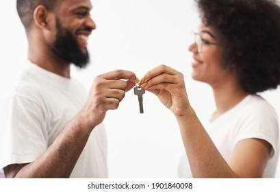 Joyful Black Couple Holding New House Key Smiling Each Other Standing Posing Over White Background Indoors, Selective Focus On Keys. Apartment Ownership, Real Estate And Family Housing Concept