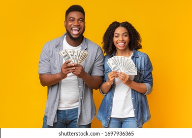 Joyful Black Couple Posing With Dollar Fans, Holding A Lot Of Money In Hands, Yellow Background With Free Space