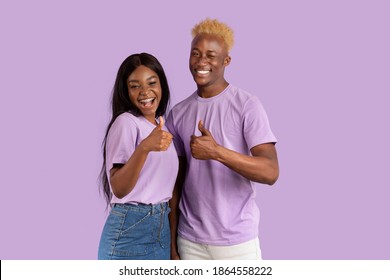 Joyful Black Couple Showing Thumbs Up Gesture, Excited About Cool Offer, Recommending Something On Violet Studio Background. Young Guy And His Girlfriend Overjoyed At Big Sale Or Discount