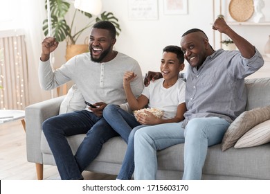 Joyful Black Family, Father, Grandfather And Son Watching Football Match On TV And Cheering, Celebrating Win Of Favorite Team, Sitting On Couch.