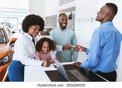 Joyful Black Family Giving Credit Card To Car Salesman, Paying For New Auto At Dealership Store. African American Customers Purchasing Automobile, Signing Agreement At Showroom