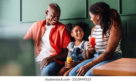 A joyful Black family shares a moment of happiness and laughter while enjoying drinks in a cozy cafe setting, epitomizing togetherness and love. - Powered by Shutterstock