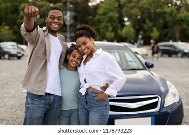 Joyful Black Family Showing New Car Key Posing Standing Near Luxury Auto Outdoor, Smiling To Camera. Parents And Daughter Celebrating Buying Vehicle. Automobile Leasing And Ownership