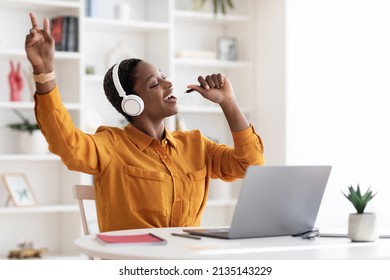 Joyful Black Female Freelancer Stylish Young Woman In Shirt Singing Karaoke At Office, Sitting At Workdesk In Front Of Laptop, Using Headset, Holding Pen As Mic, Copy Space. Stress Relief Concept