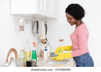 Joyful Black Lady Housewife Washing Dishes And Smiling, Wearing Colorful Rubber Gloves, Using Sponge, Copy Space. Young African American Woman House-keeper Or Made Cleaning House