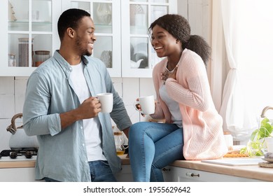 Joyful Black Lovers Having Fun Together While Drinking Coffee In Kitchen. Romantic Young African American Couple Chatting And Laughing At Home Interior, Enjoying Hot Drinks And Domestic Relax