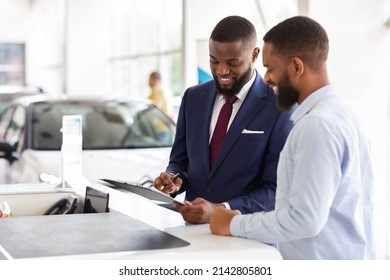 Joyful Black Man Buying Car, Signing Papers With Salesman In Dealership Office, Happy Young African American Male Consulting With Manager While Purchasing New Vehicle In Modern Showroom, Copy Space