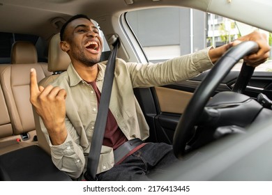 Joyful black man dancing in car, singing while driving his car. Road fun