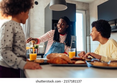 A joyful black mom is pouring orange juice to her daughters over breakfast at home - Powered by Shutterstock