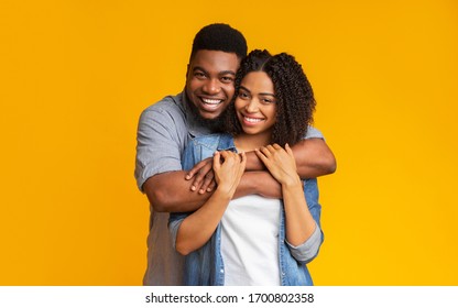 Joyful black sweethearts hugging and posing to camera, standing together over yellow background in studio, copy space