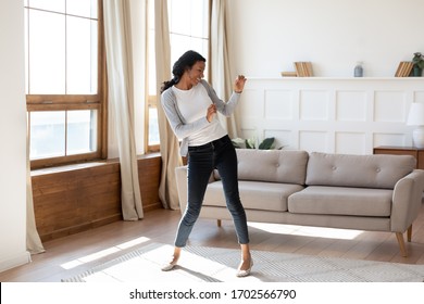 Joyful Black Young Woman Dancing In Bright Modern Living Room. Happy Girl Have Fun At Home On Lazy Weekend, Receive Good Or Pleasant News, Celebrate Moving To New Apartment Or House