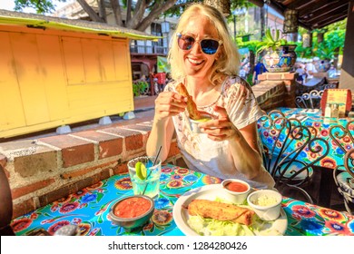 Joyful Blonde Woman Puts Enchilada In Chili Sauce, At Typical Mexican Food, At Traditional Restaurant Of El Pueblo, Olvera Street, Los Angeles Downtown State Historic Park, California, United States.