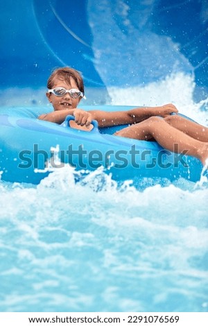 Joyful boy descends on an inflatable circle from the water slide in the water park, children's attractions in the water park, water slides, children's entertainment on vacation