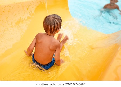 Joyful boy descends from the water slide in the water park, children's attractions in the water park, water slides, children's entertainment on vacation
