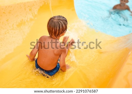 Joyful boy descends from the water slide in the water park, children's attractions in the water park, water slides, children's entertainment on vacation