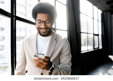 A joyful Brazilian businessman checks his smartphone in a bright, modern office, showcasing a moment of connectivity and modern work life. Male entrepreneur using mobile phone indoor - Powered by Shutterstock