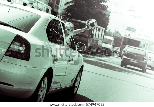 Joyful bride leaned out of the window on the go\
white car reached out with a wedding bouquet of white flowers,\
roses. Girl dressed in white lace wedding dress and a gold ring.\
Black and White\'s photos
