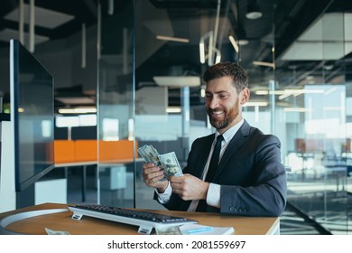Joyful business man in sitting at desk working on laptop computer in bright office Achieving business career concept. Keep cash by making a gesture to the winner