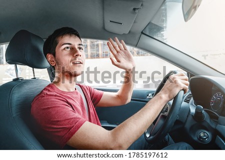 Joyful and careless car driver raises his hand in thanks for giving way. Traffic rules and politeness concept